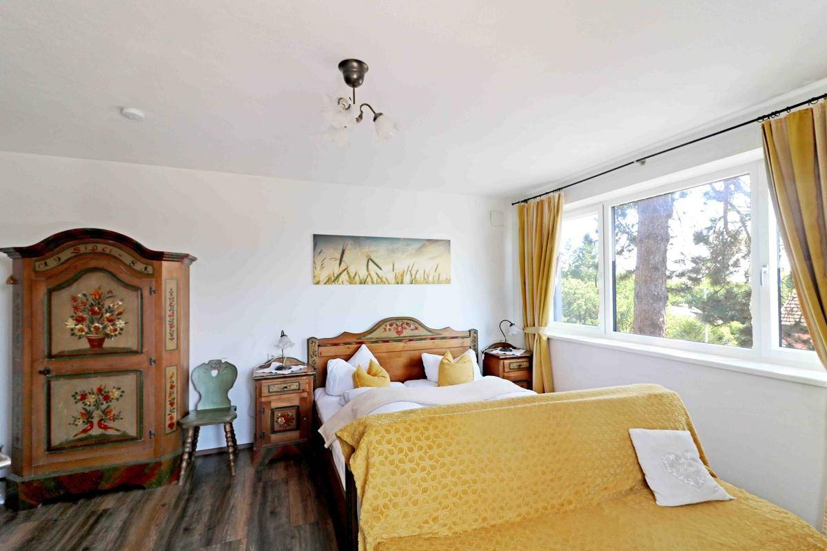 Helles Schlafzimmer mit einem Doppelbett, einem bemalten Holzschrank und einem großen Fenster mit Blick ins Grüne.