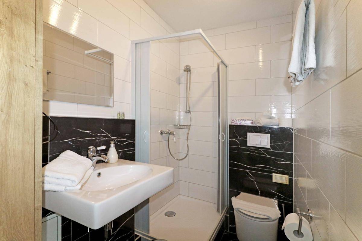 Modernes Badezimmer mit Duschkabine, Waschbecken und Toilette, ausgestattet mit weißen und schwarzen Fliesen.