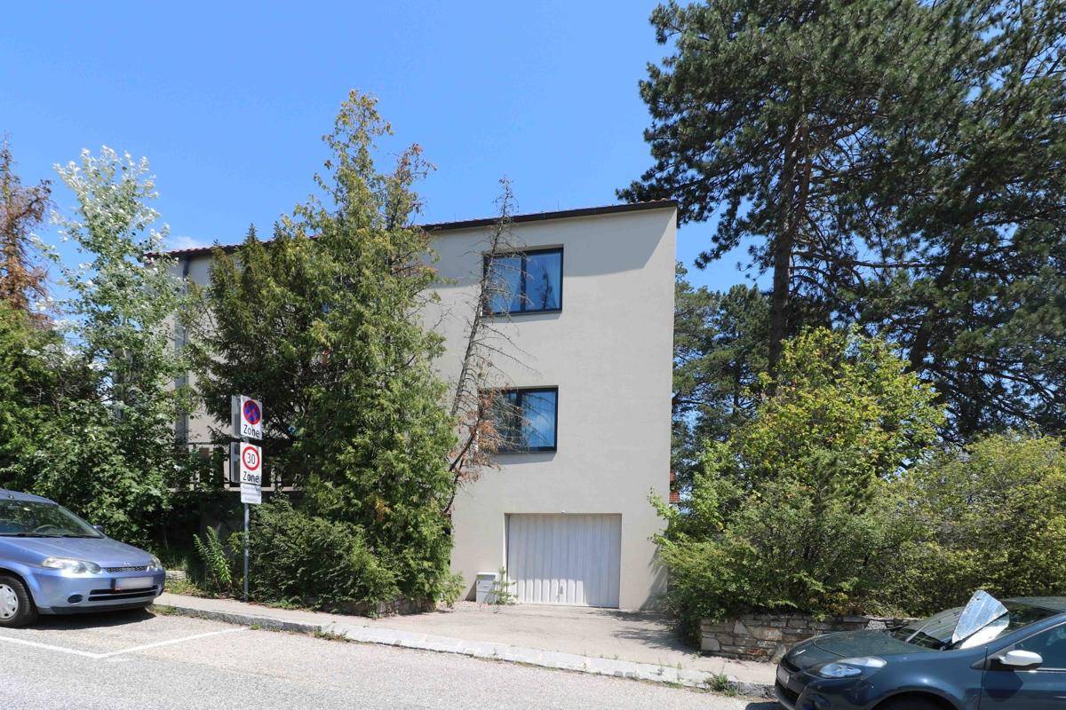 Seitenansicht des Gebäudes mit einer Garage im Erdgeschoss und umgebender Vegetation.