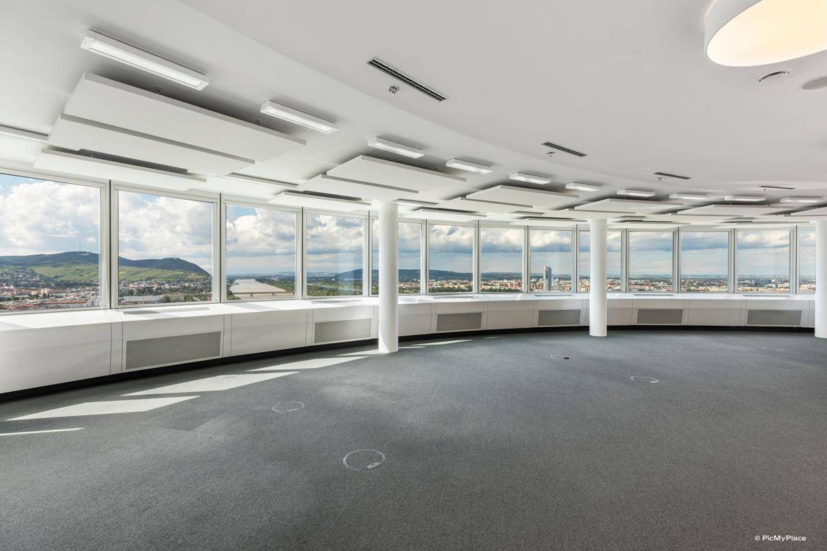 Heller Büroraum mit Teppichboden und einer durchgehenden Fensterfront, die einen Panoramablick ermöglicht.