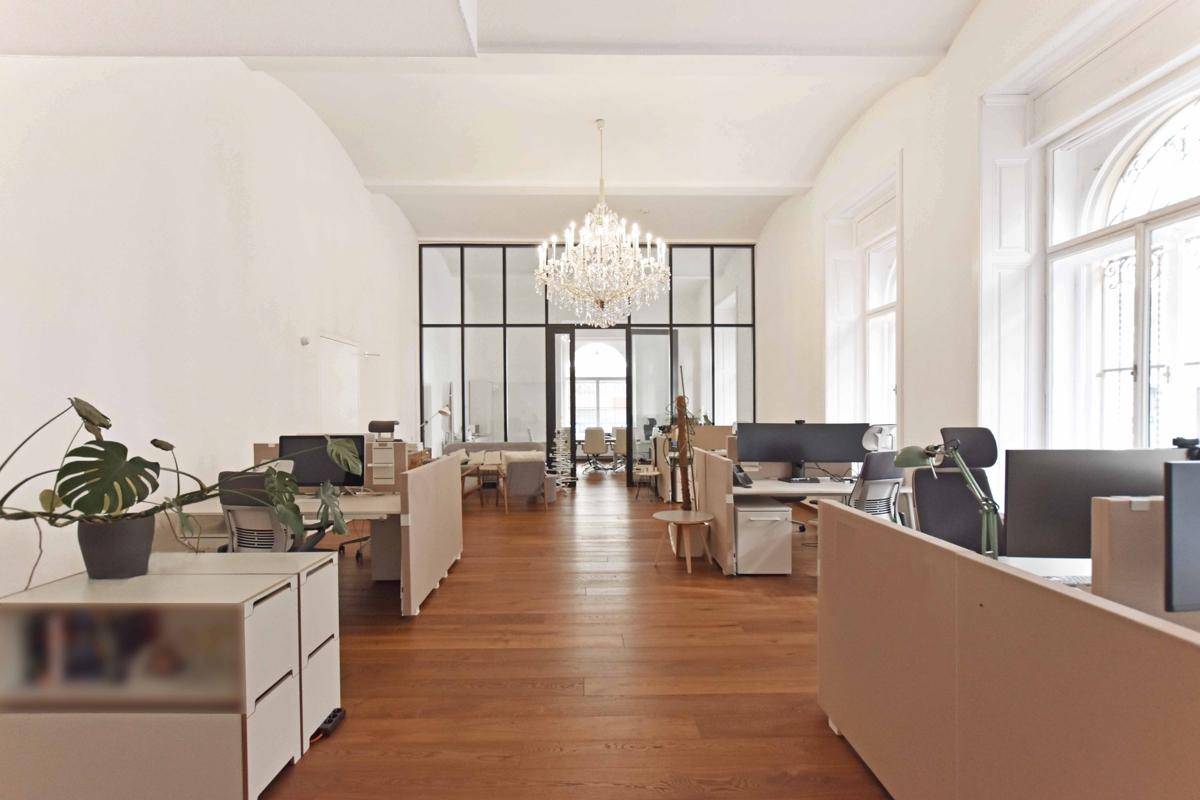 Geräumiges Großraumbüro mit Holzboden, hohen Decken und einem eleganten Kronleuchter, der den Raum erhellt.