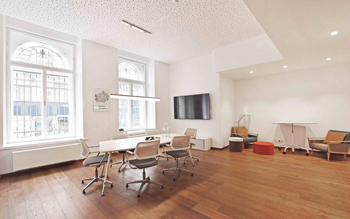 Moderner Besprechungsraum mit Holzboden, großen Fenstern und einem Flachbildschirm, ideal für Präsentationen.