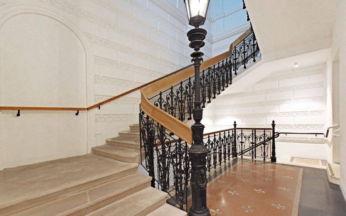 Elegantes Treppenhaus mit kunstvollem Geländer und historischem Charme, beleuchtet von einer klassischen Laterne.