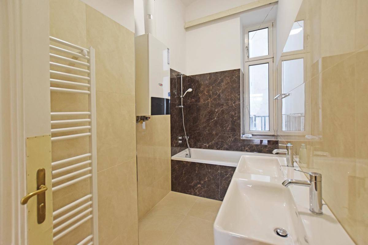 Modernes Badezimmer mit doppelten Waschbecken, Badewanne mit Duschfunktion und Fenster für Tageslicht.