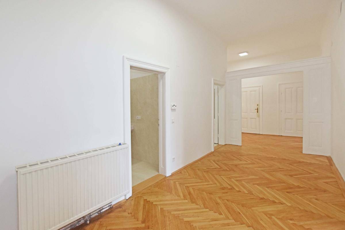 Flur mit Fischgrätparkett und Heizkörper, der den Zugang zu einem Badezimmer ermöglicht.