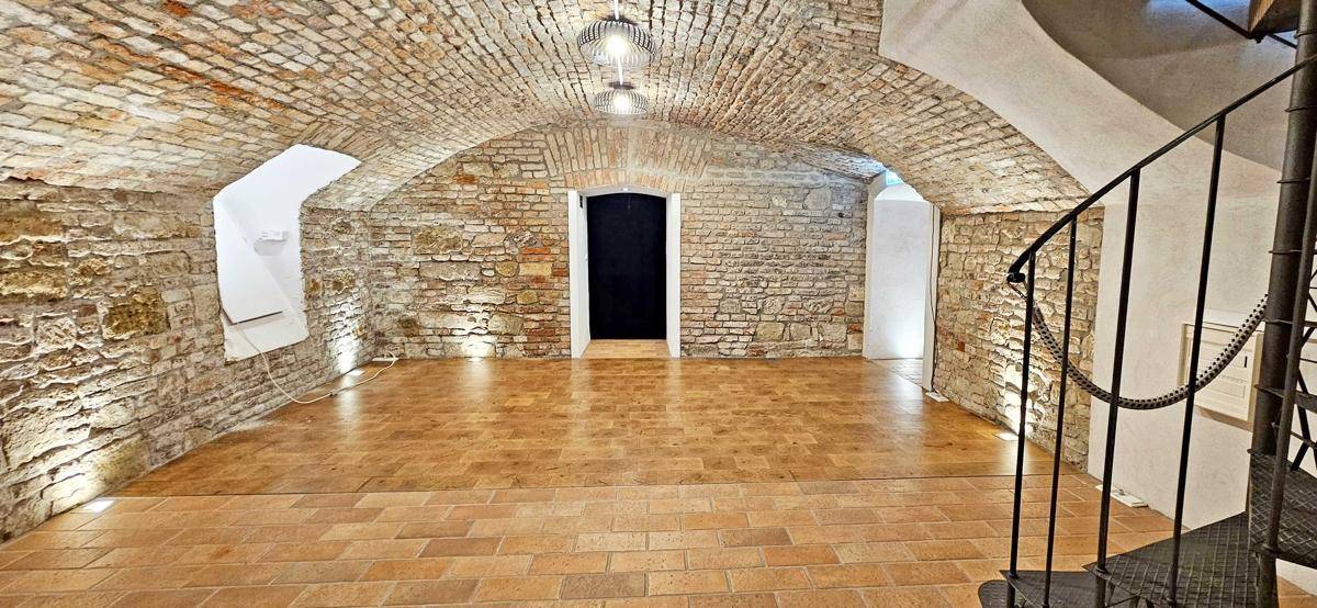 Historischer Gewölbekeller mit freigelegten Ziegelwänden, Terrakottaboden und einer eleganten Wendeltreppe.
