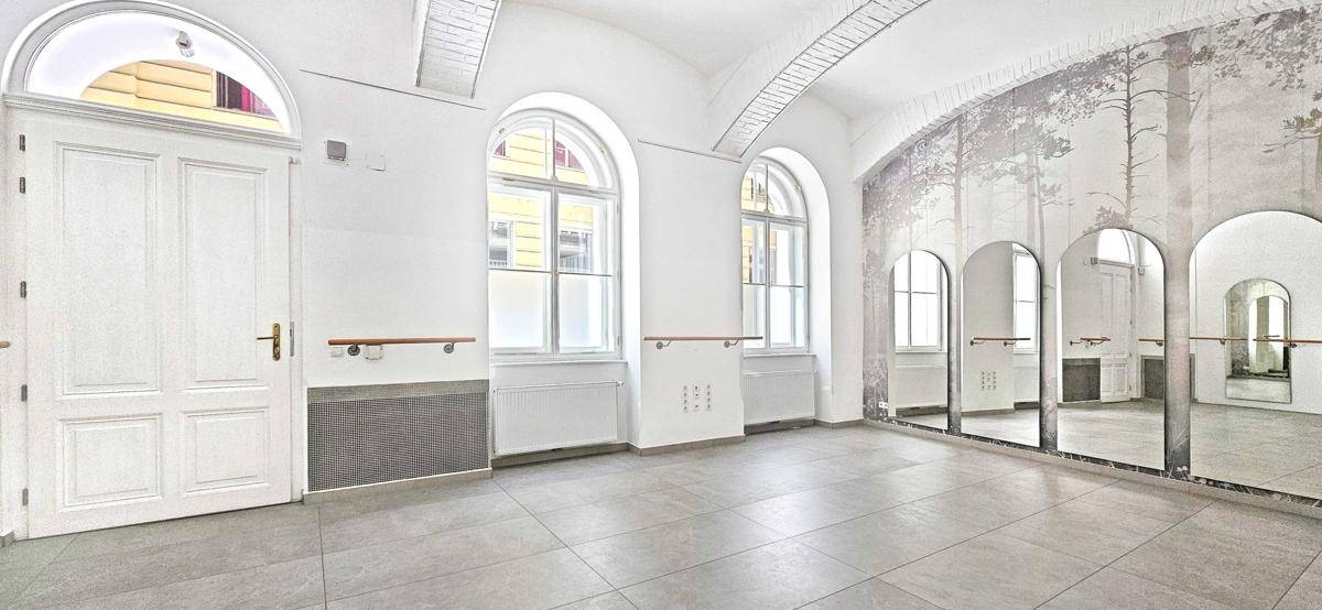 Geräumiger Raum mit hohen Rundbogenfenstern, Spiegelwand und modernem Fliesenboden, sehr hell.