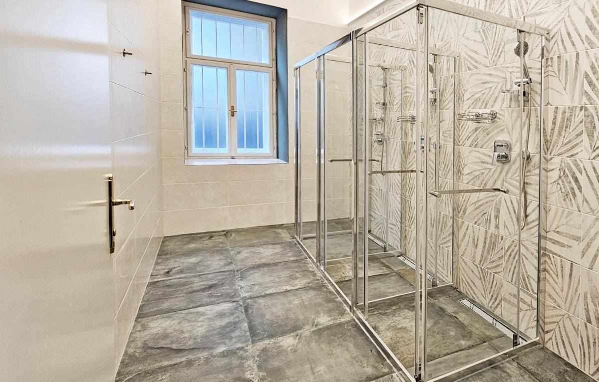 Modernes Badezimmer mit mehreren Duschkabinen, gemusterten Fliesen und Fenster für natürliches Licht.