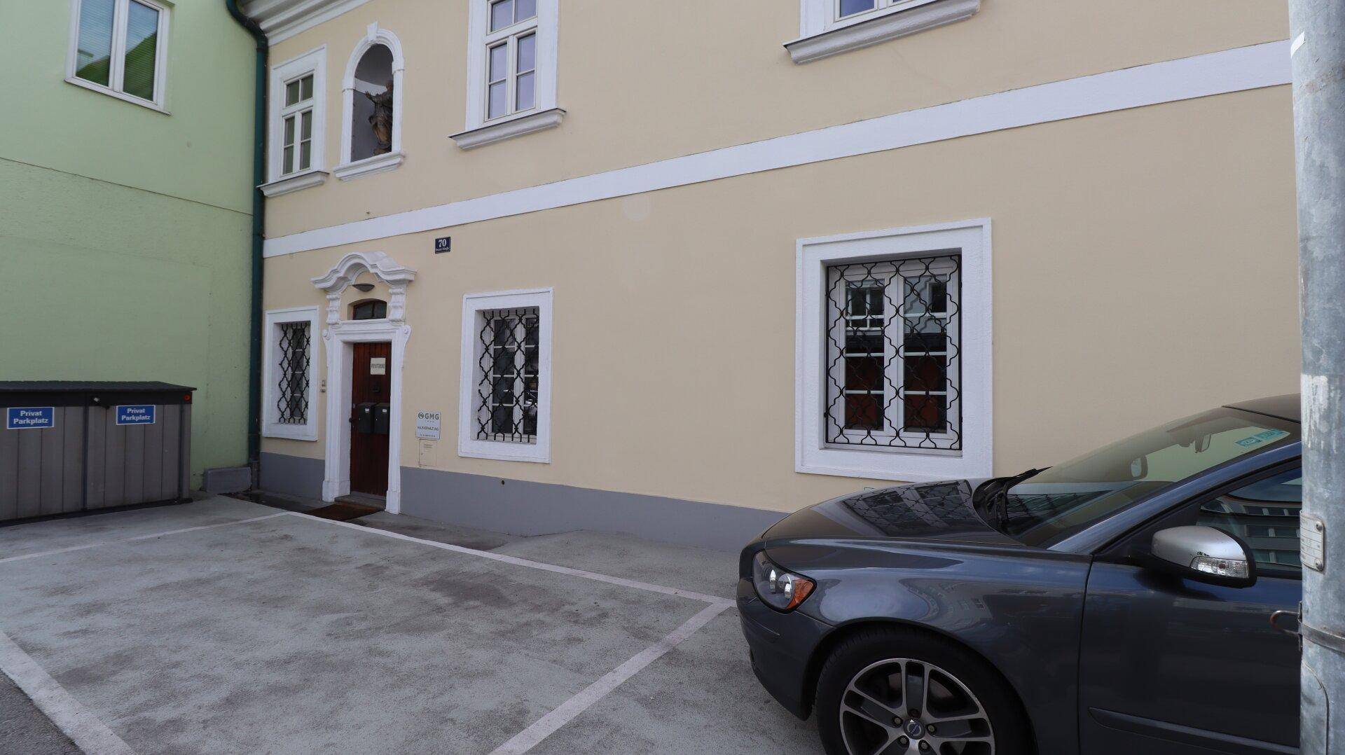 Gebäudefassade eines Altbaus mit klassischer Architektur und einem Parkplatz davor.