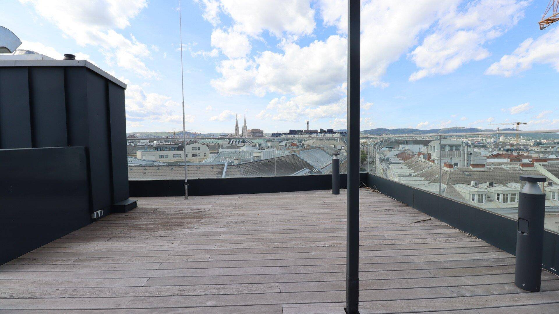 Geräumige Dachterrasse mit Holzboden und weitem Blick über die Stadt.