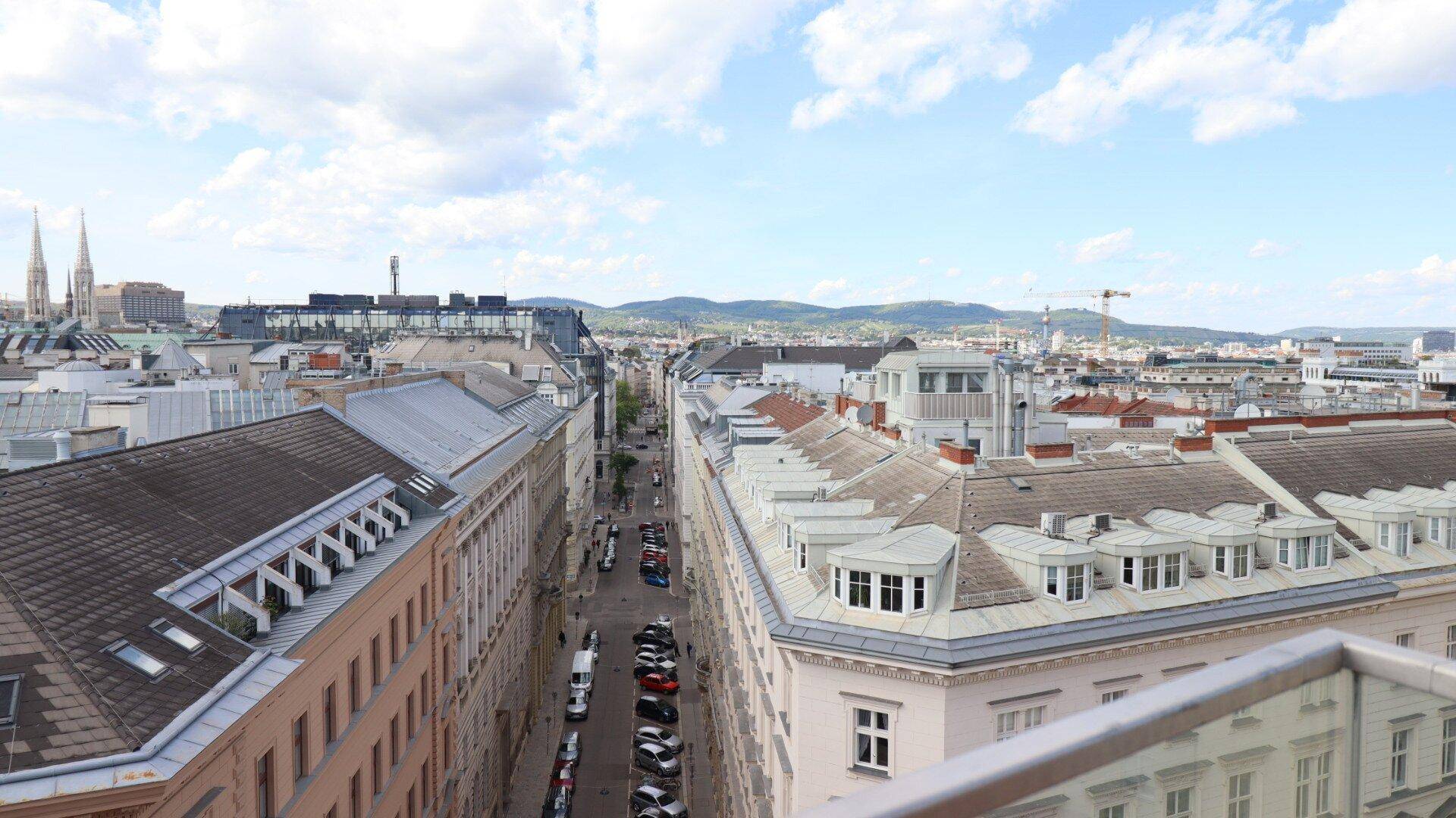 Blick von oben auf eine belebte Stadtstraße mit historischen Gebäuden und parkenden Autos.