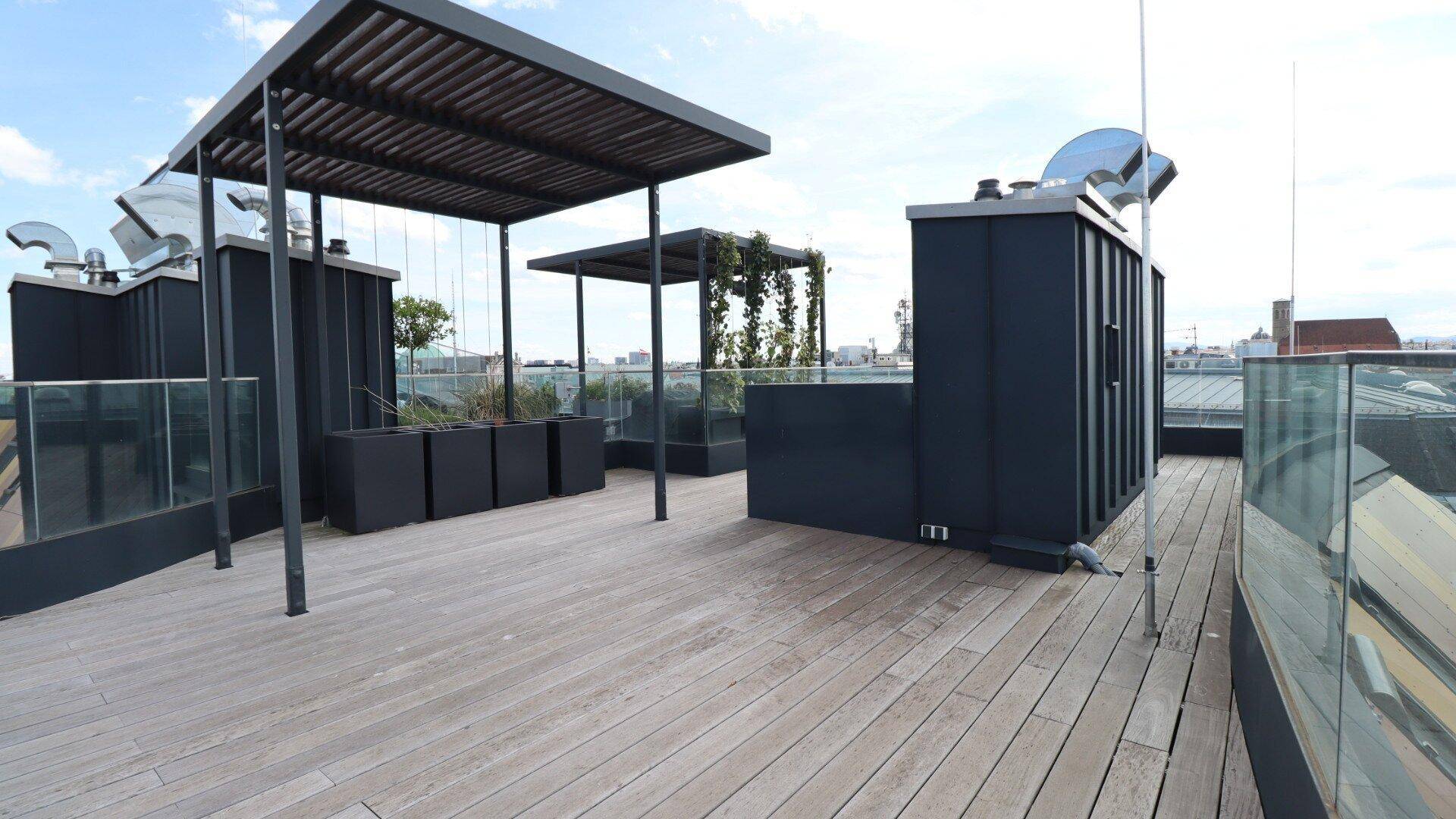 Moderne Dachterrasse mit Holzdeck, Pergolen und Pflanzenkübeln, ideal für Entspannung.