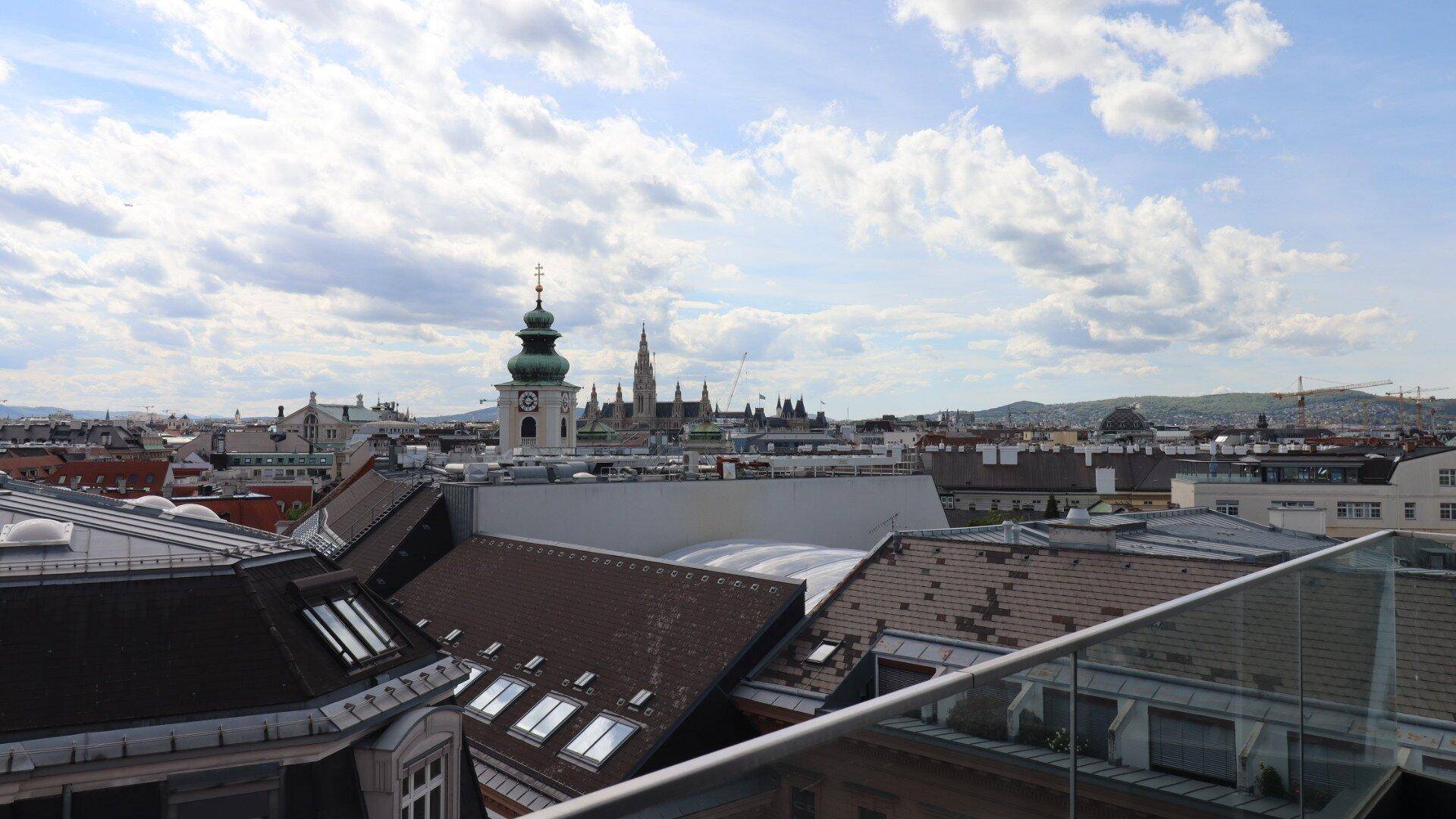 Weitläufiger Blick über die Dächer der Stadt mit markanten Kirchtürmen unter blauem Himmel.