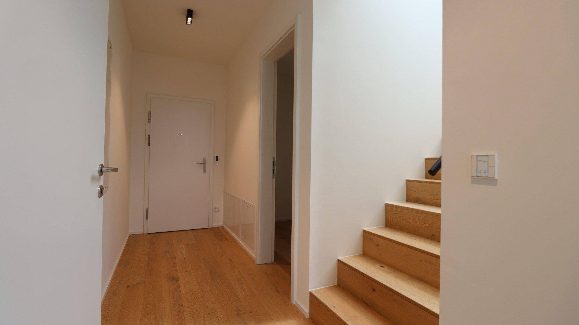 Heller Flur mit Holztreppe und Eingangstür.