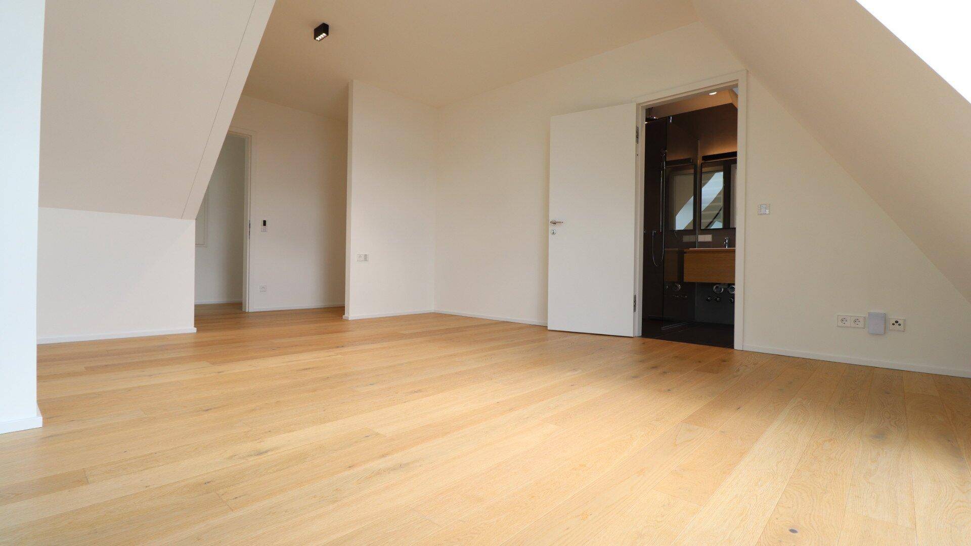 Helles Schlafzimmer im Dachgeschoss mit Zugang zu einem modernen Badezimmer.