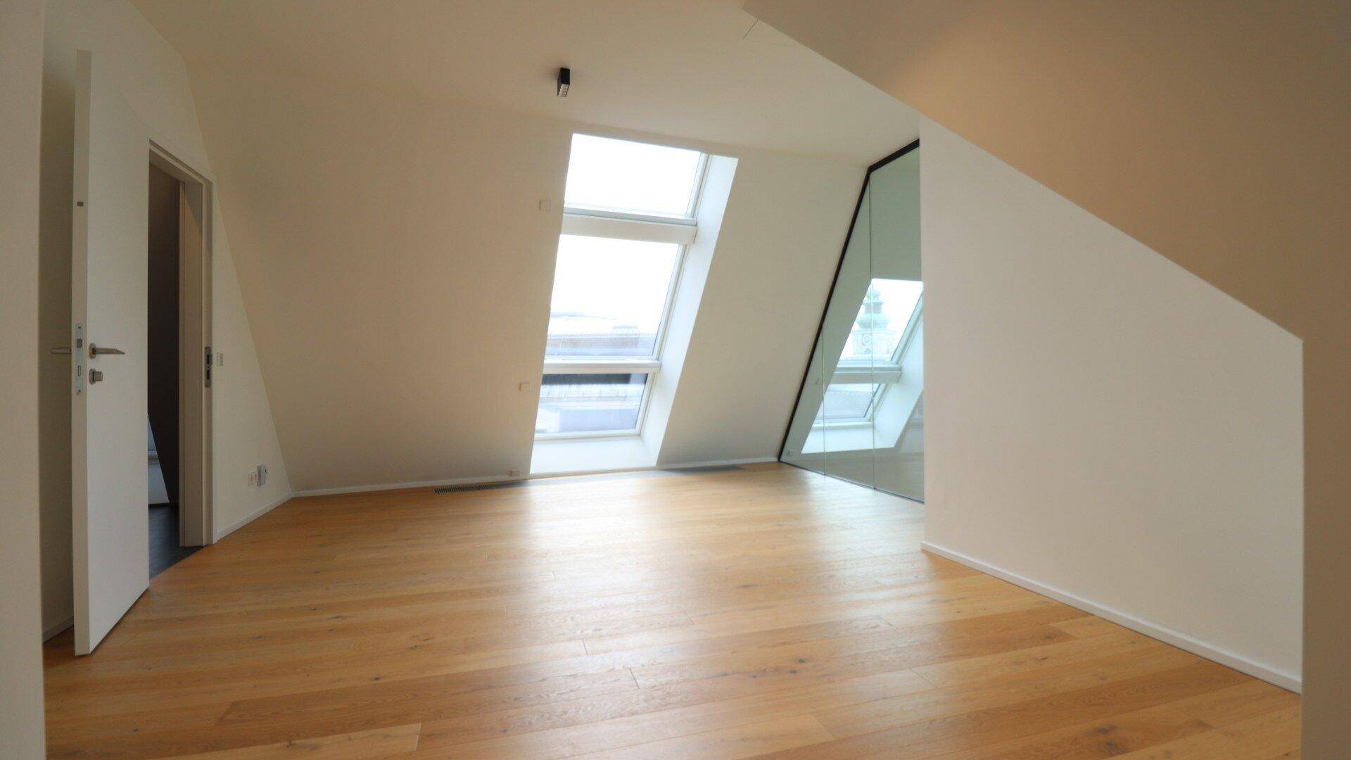 Helles Zimmer im Dachgeschoss mit Holzparkettboden und Dachfenstern.