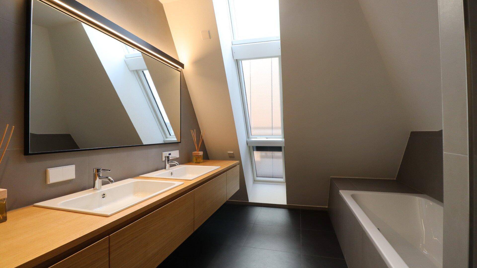 Modernes Badezimmer mit Doppelwaschbecken, Badewanne und viel Tageslicht durch Dachfenster.