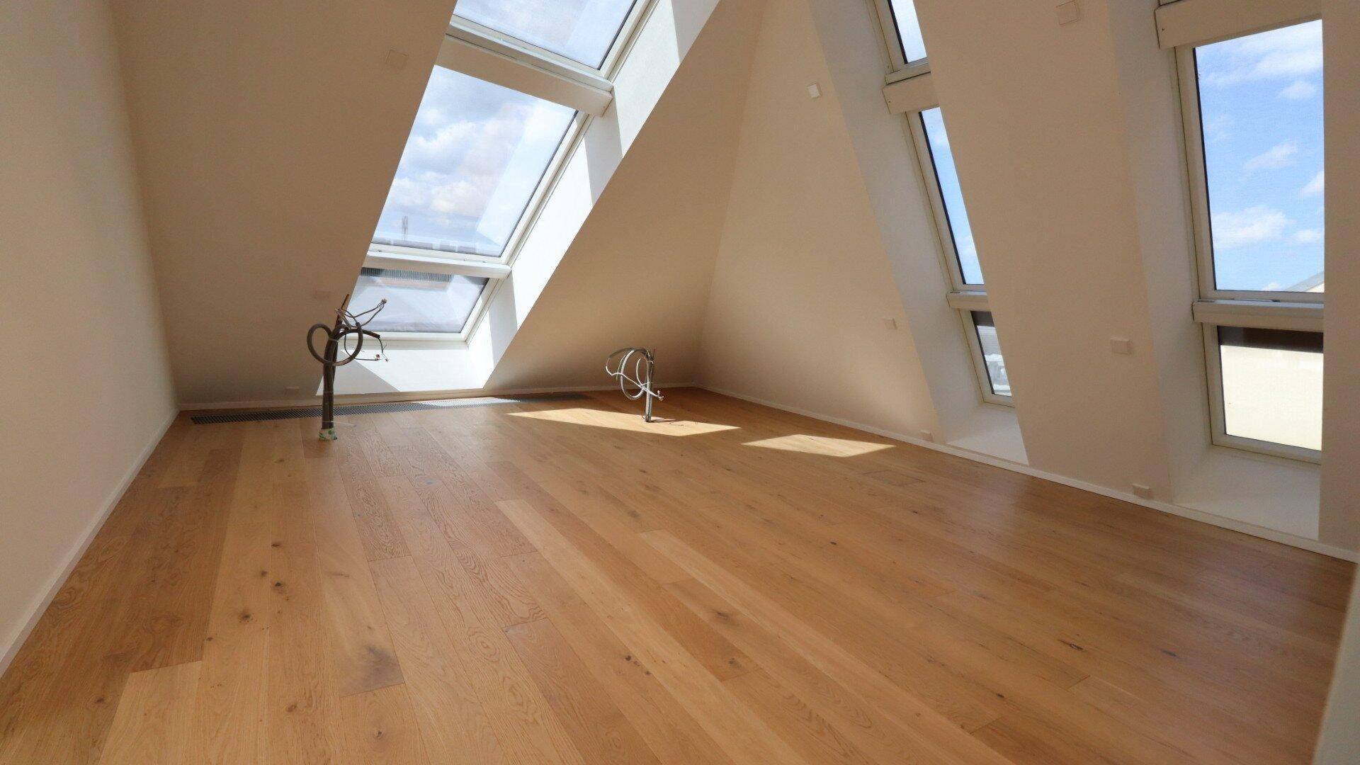 Geräumiges Zimmer im Dachgeschoss mit großen Dachfenstern und hellem Holzparkett.