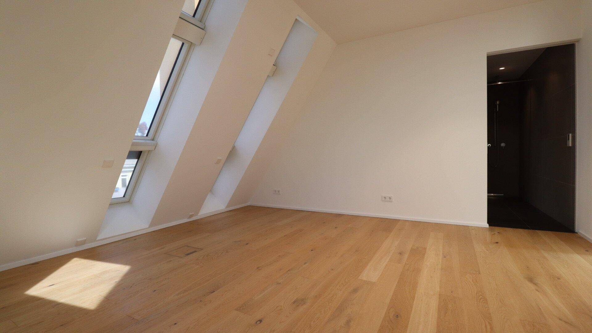 Helles Schlafzimmer im Dachgeschoss mit Dachfenster und Zugang zu einem modernen Badezimmer.