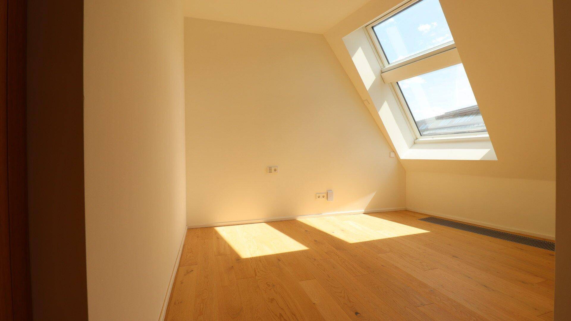 Helles Schlafzimmer im Dachgeschoss mit Holzparkett und großem Dachfenster.