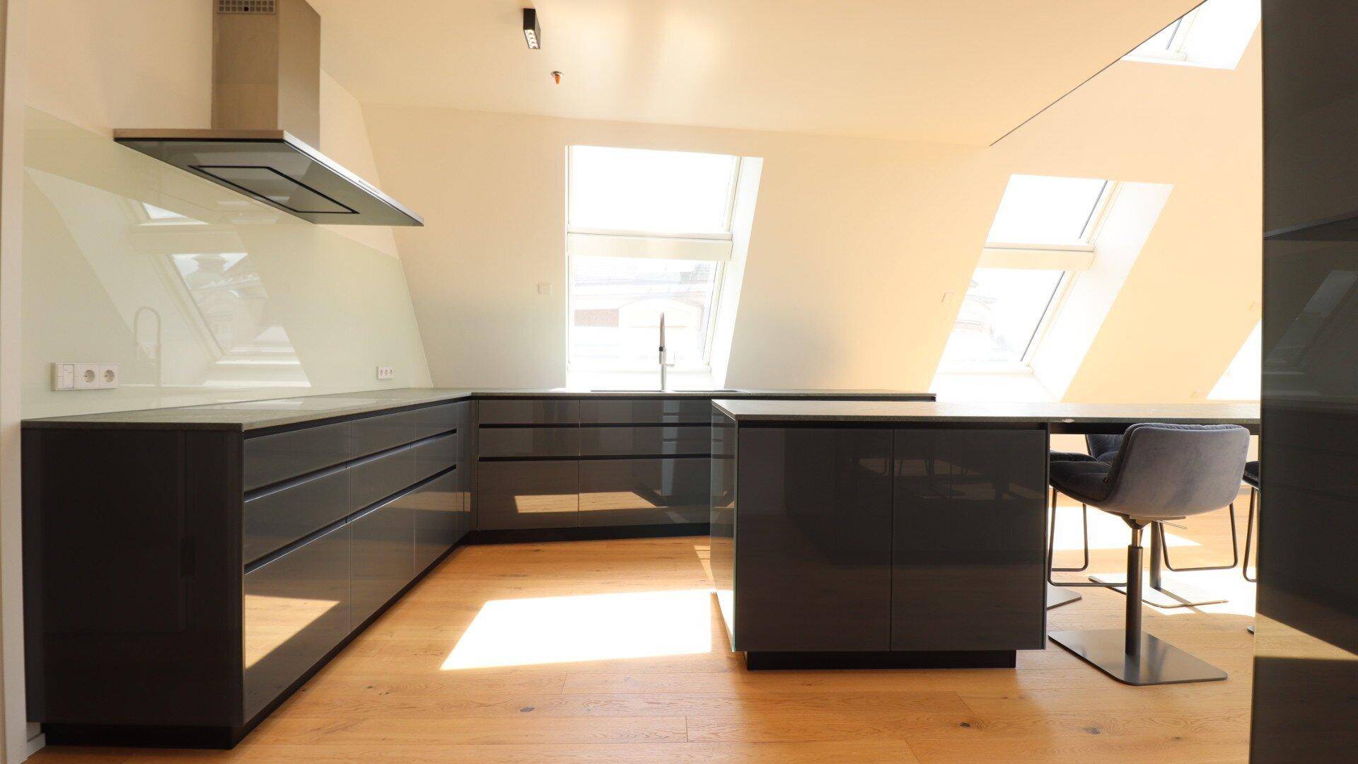 Elegante, moderne Küche mit grauen Hochglanzfronten, Dunstabzugshaube und hellem Holzfußboden.