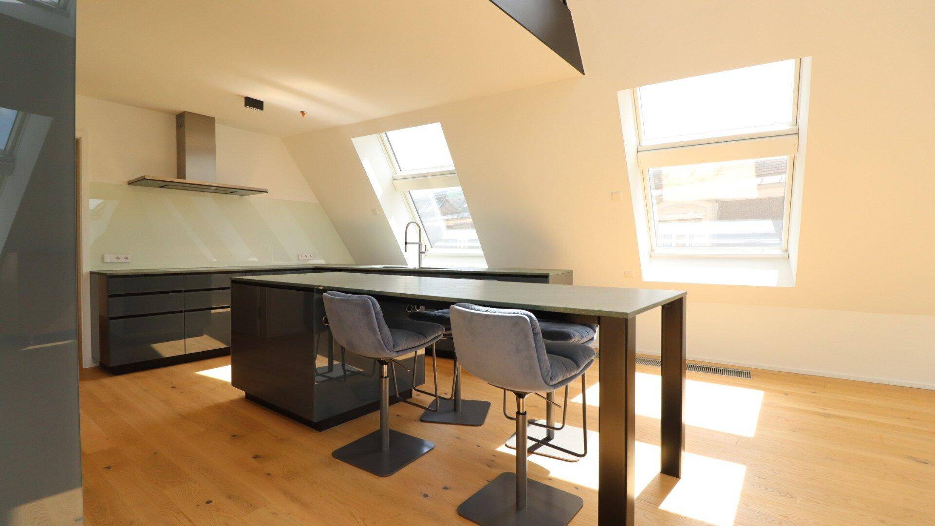 Moderne Küche im Dachgeschoss mit grauen Schränken, Kochinsel und viel Tageslicht durch Dachfenster.