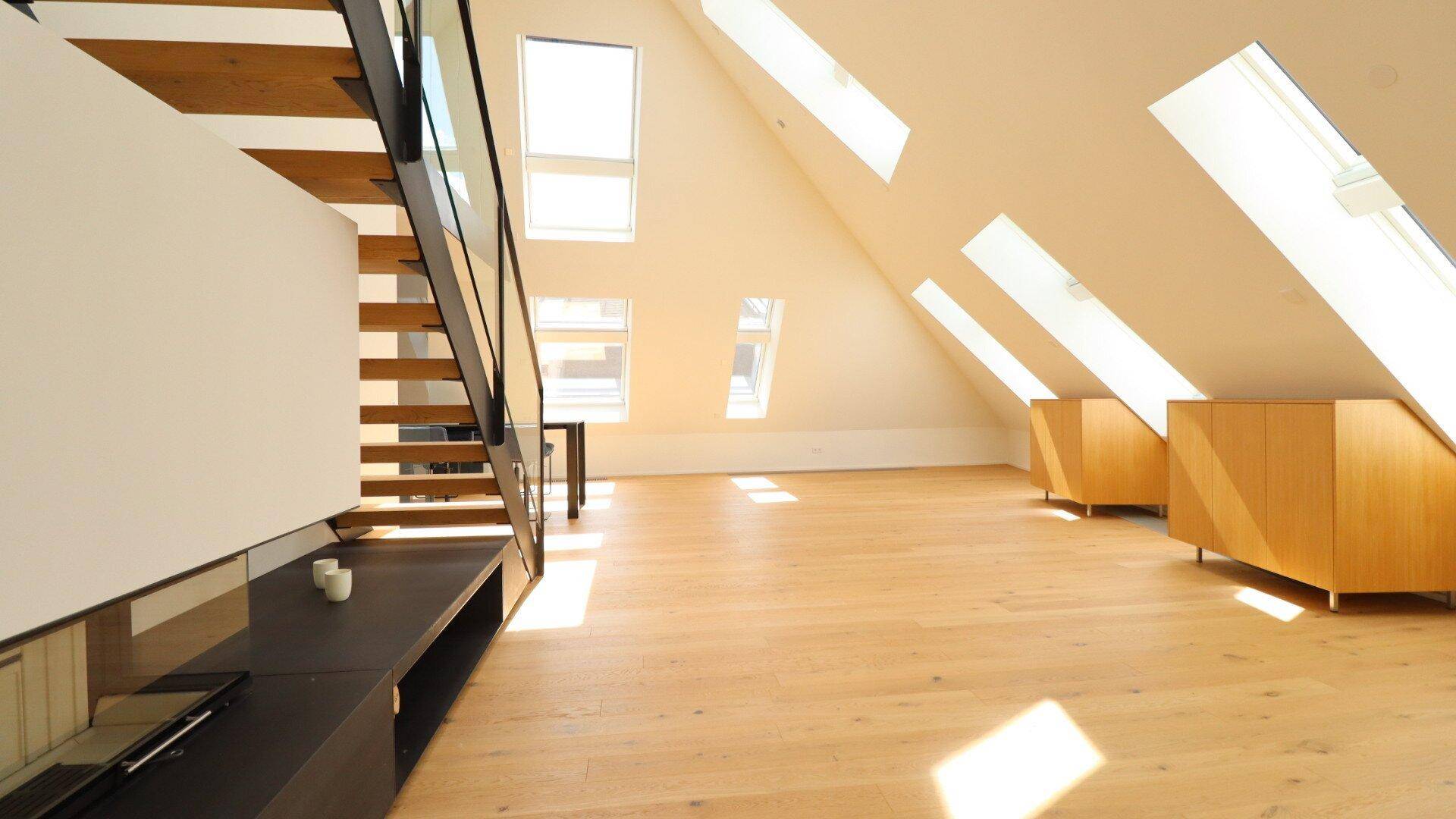 Geräumiges Dachgeschoss-Wohnzimmer mit Holzboden, Dachfenstern und modernen Holzschränken.
