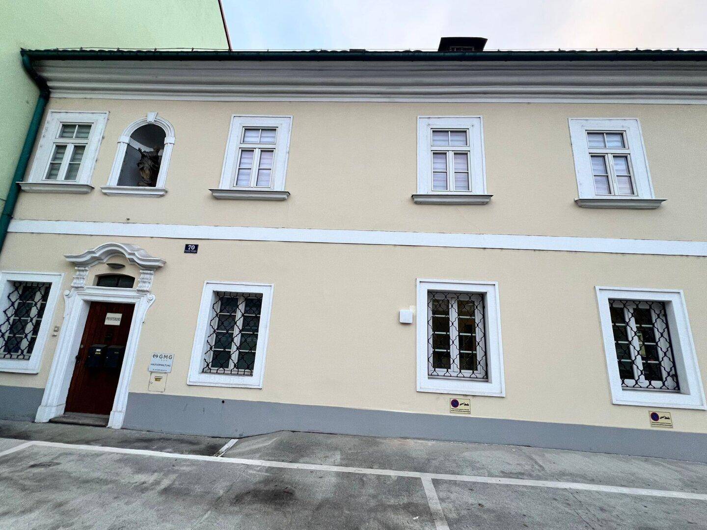 Historisches Gebäude mit beiger Fassade, weißen Fensterrahmen und einem verzierten Eingang.