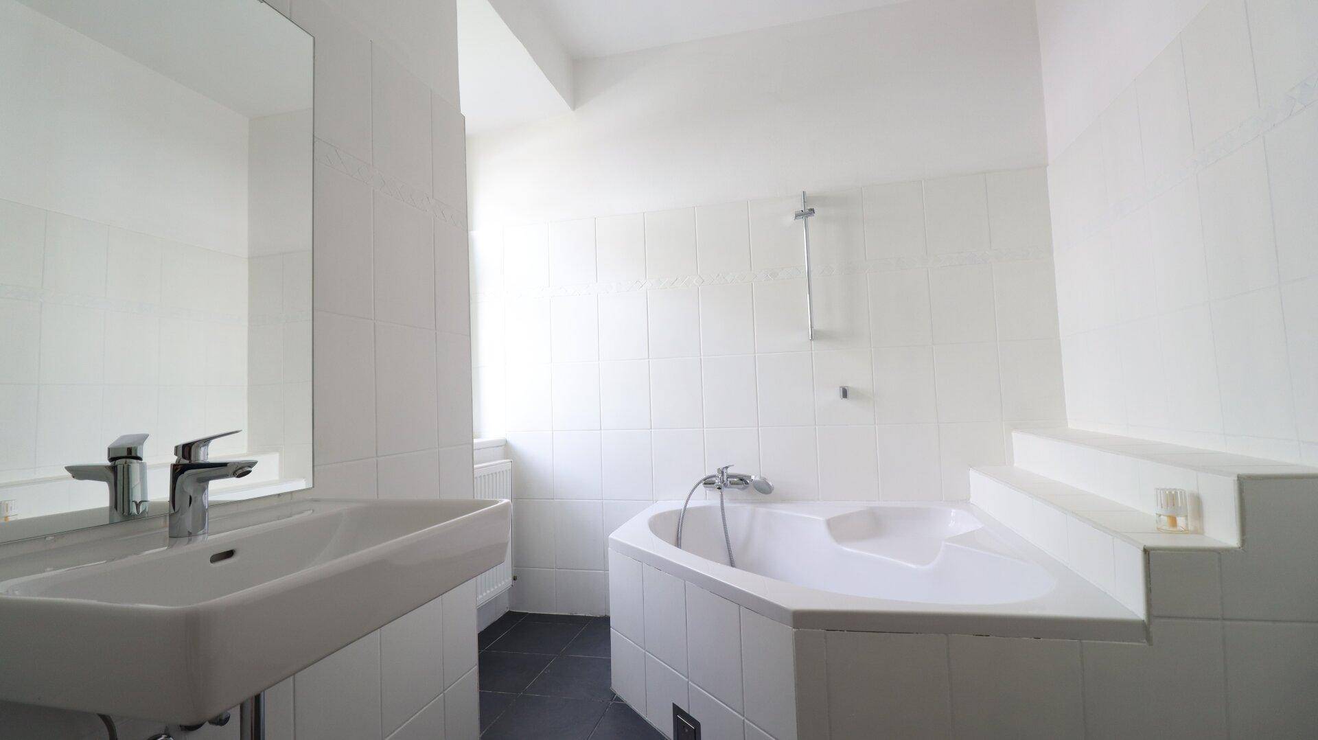Modernes Badezimmer mit Eckbadewanne, weißen Wandfliesen und einem einzelnen Waschbecken.