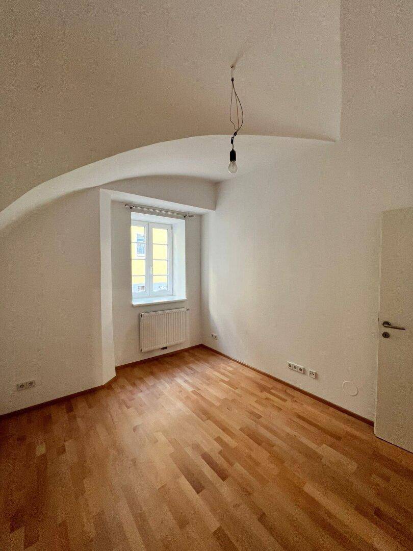 Geräumiges Schlafzimmer mit Gewölbedecke, Holzboden und einem Fenster, das viel Licht hereinlässt.