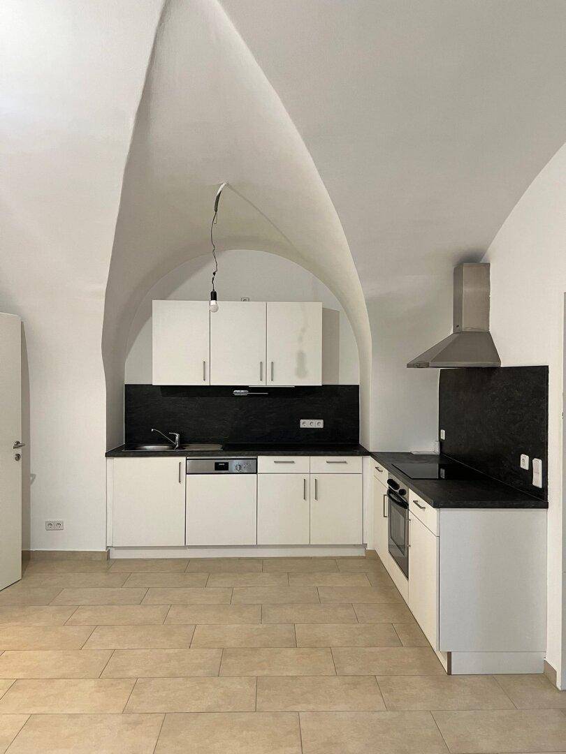 Moderne Einbauküche mit weißen Schränken, schwarzer Arbeitsplatte und beeindruckender Gewölbedecke.