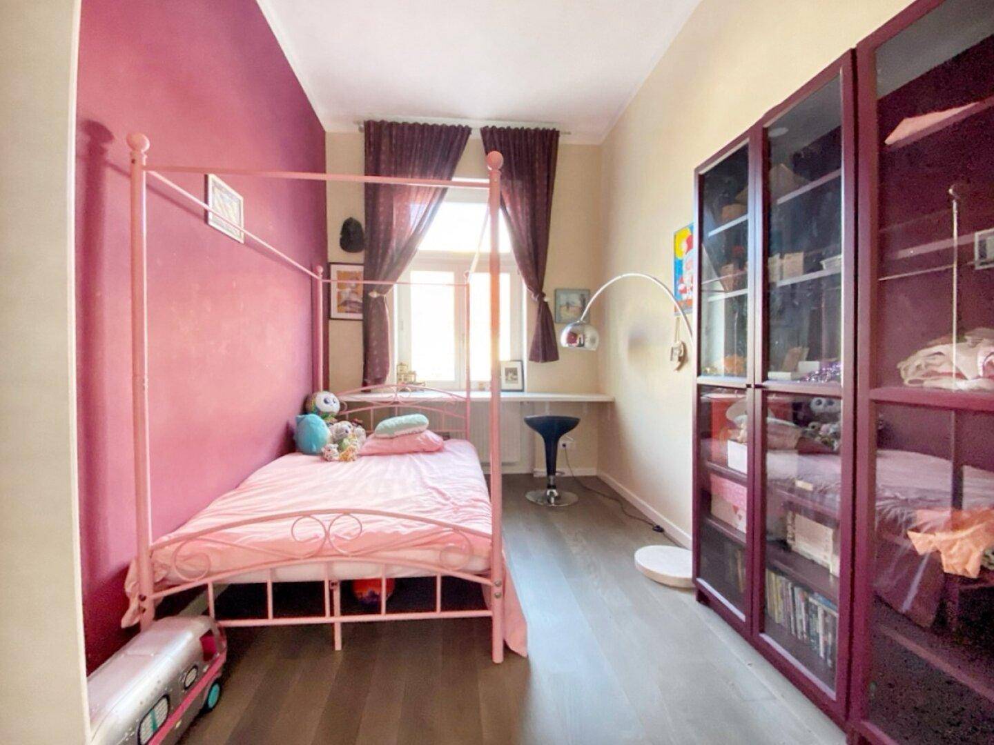 Kinderzimmer mit rosa Himmelbett, farbiger Wandgestaltung und dunklem Holzboden.