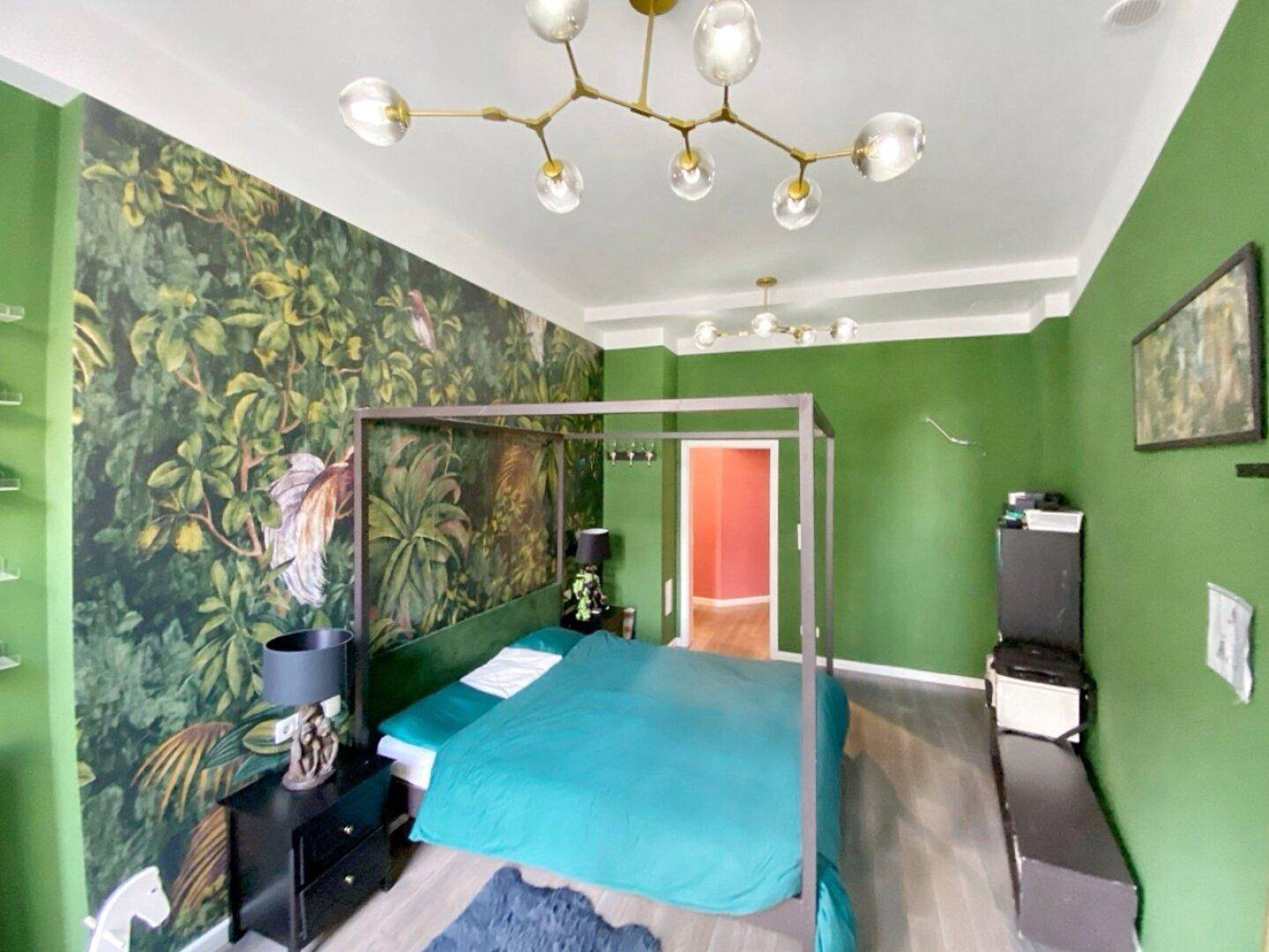 Schlafzimmer mit Himmelbett, grünen Wänden und auffälliger tropischer Mustertapete.