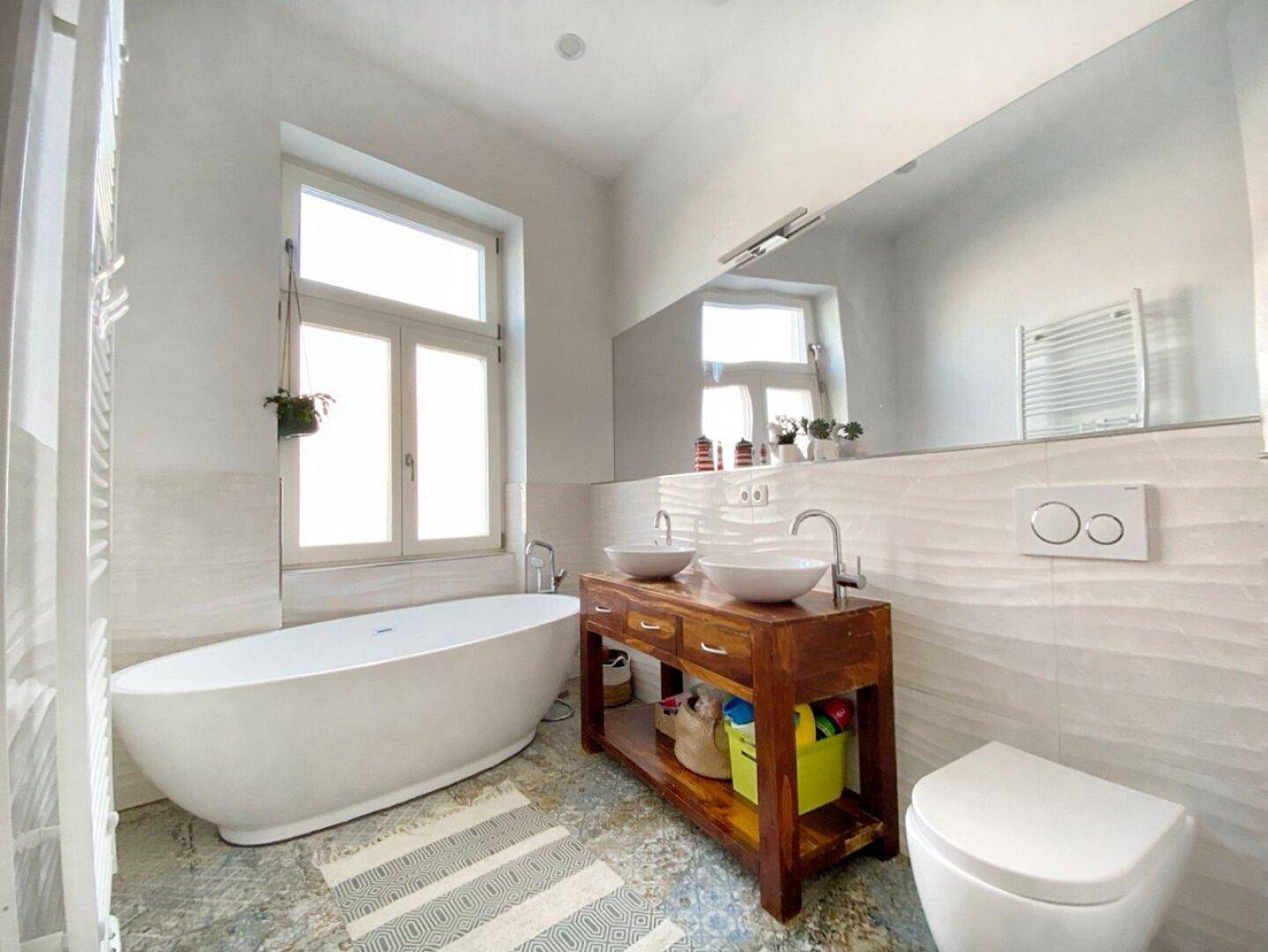 Geräumiges Badezimmer mit freistehender Badewanne, Doppelwaschbecken und großem Fenster.