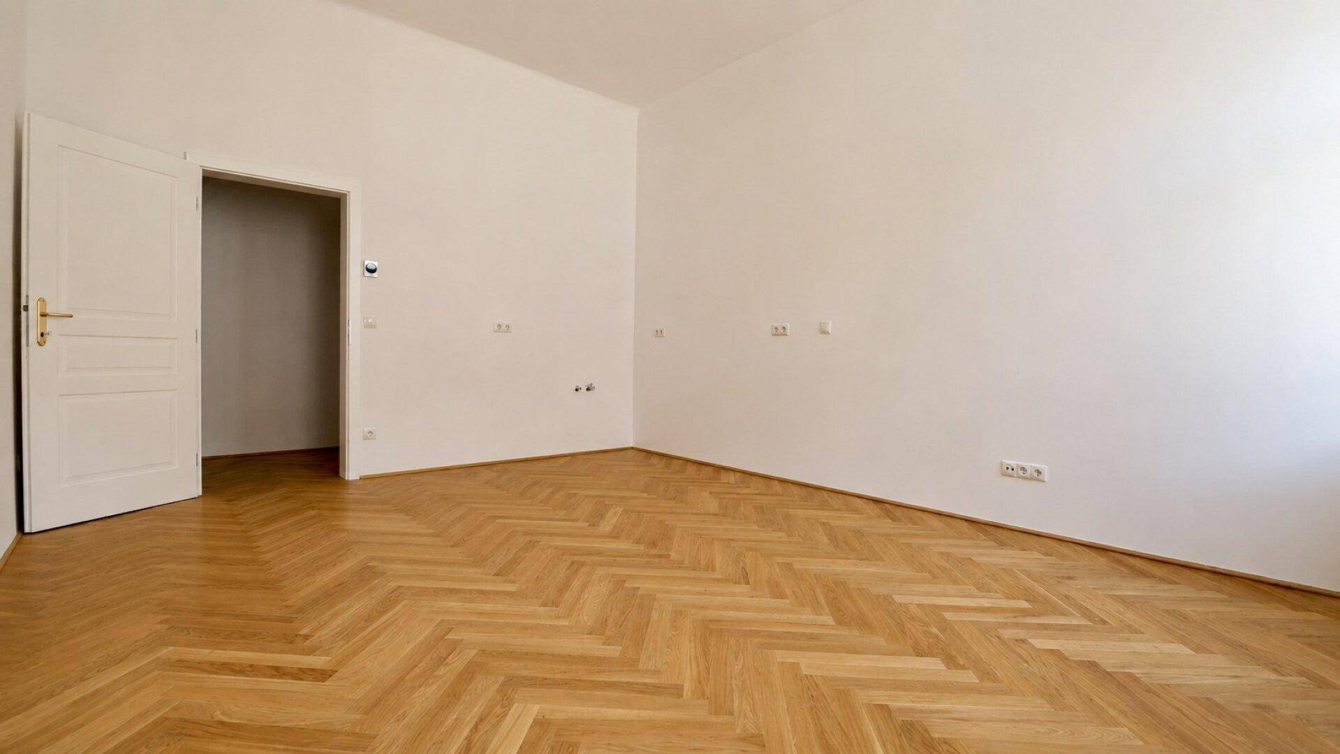 Geräumiges Zimmer mit klassischem Fischgrätparkett und Zugang zu weiteren Räumen.