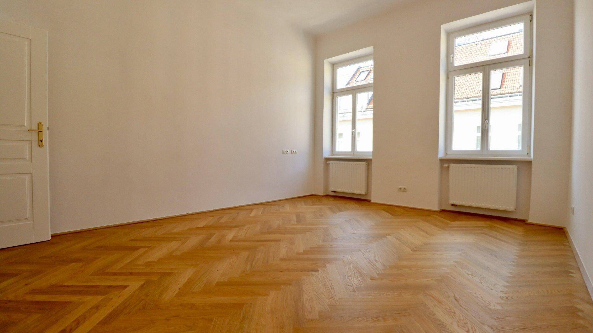 Helles Zimmer mit Fischgrätparkett und Fenstern, die einen Blick auf die Dächer bieten.