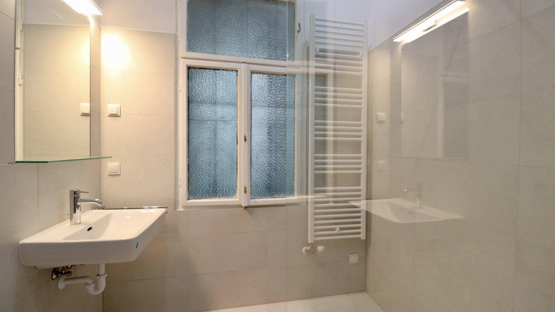 Modernes Badezimmer mit Waschbecken, beheiztem Handtuchhalter und Fenster für Tageslicht.
