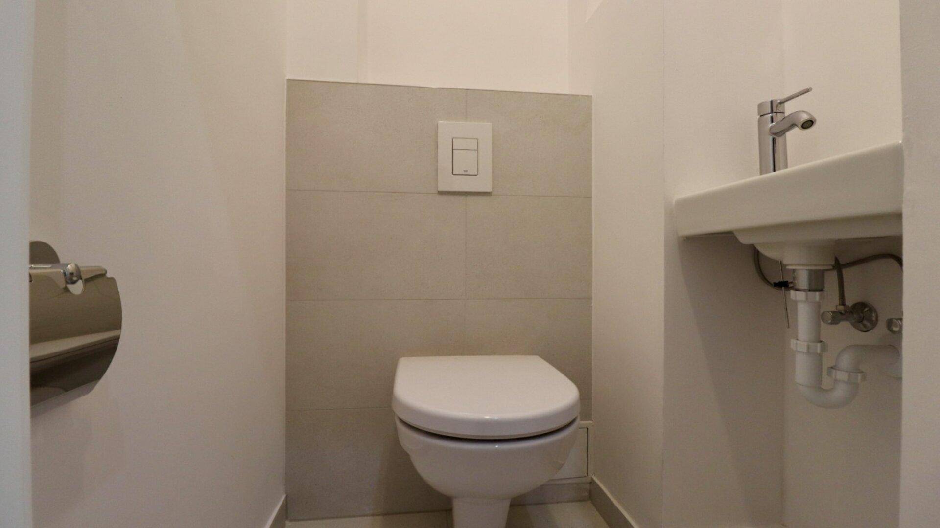 Kompaktes Gäste-WC mit wandhängender Toilette und kleinem Handwaschbecken.