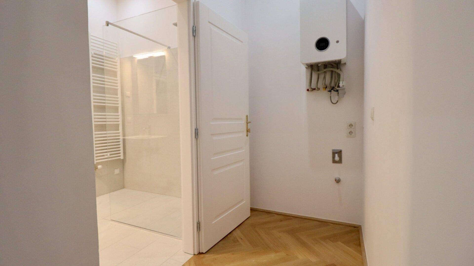 Flur mit Heiztherme und Zugang zum modernen Duschbereich mit Glasabtrennung.