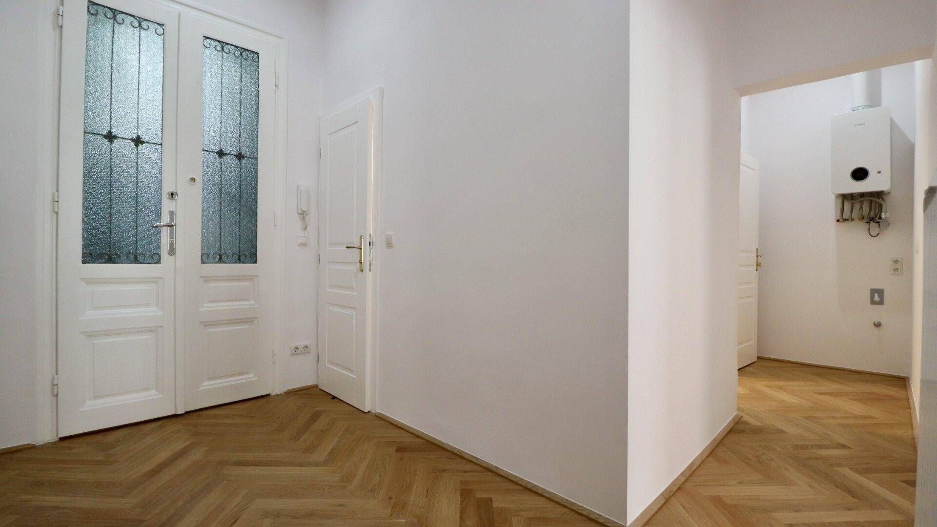 Heller Flur mit Fischgrätparkett und eleganten Doppeltüren mit Glaseinsätzen.