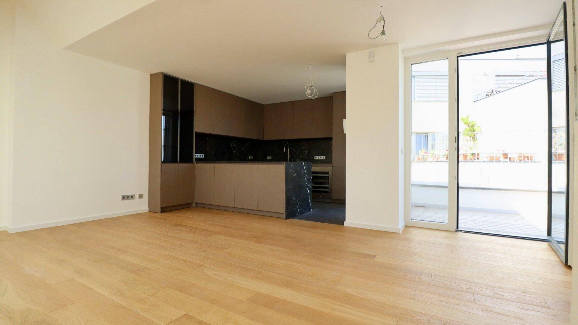 Heller offener Wohnbereich mit Holzboden und integrierter moderner Küche mit Terrassenzugang.