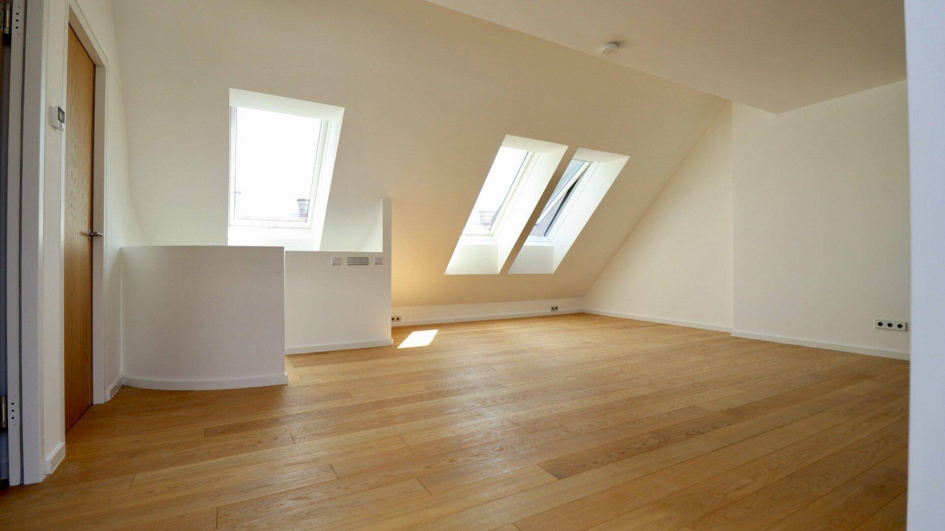 Geräumiger Wohnbereich im Dachgeschoss mit Holzboden, Dachschrägen und viel natürlichem Licht durch die Fenster.