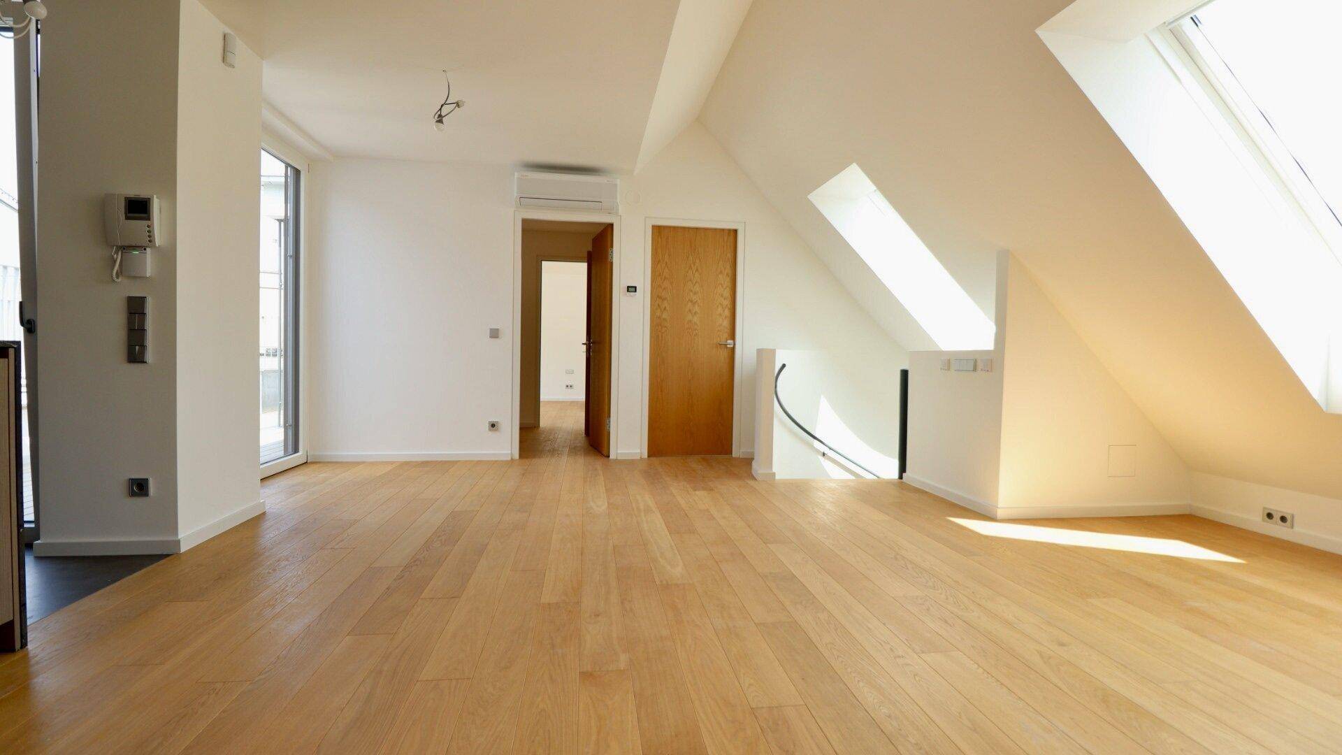 Offener Wohnbereich mit Holzboden, Zugang zu weiteren Räumen und einer eleganten Wendeltreppe.