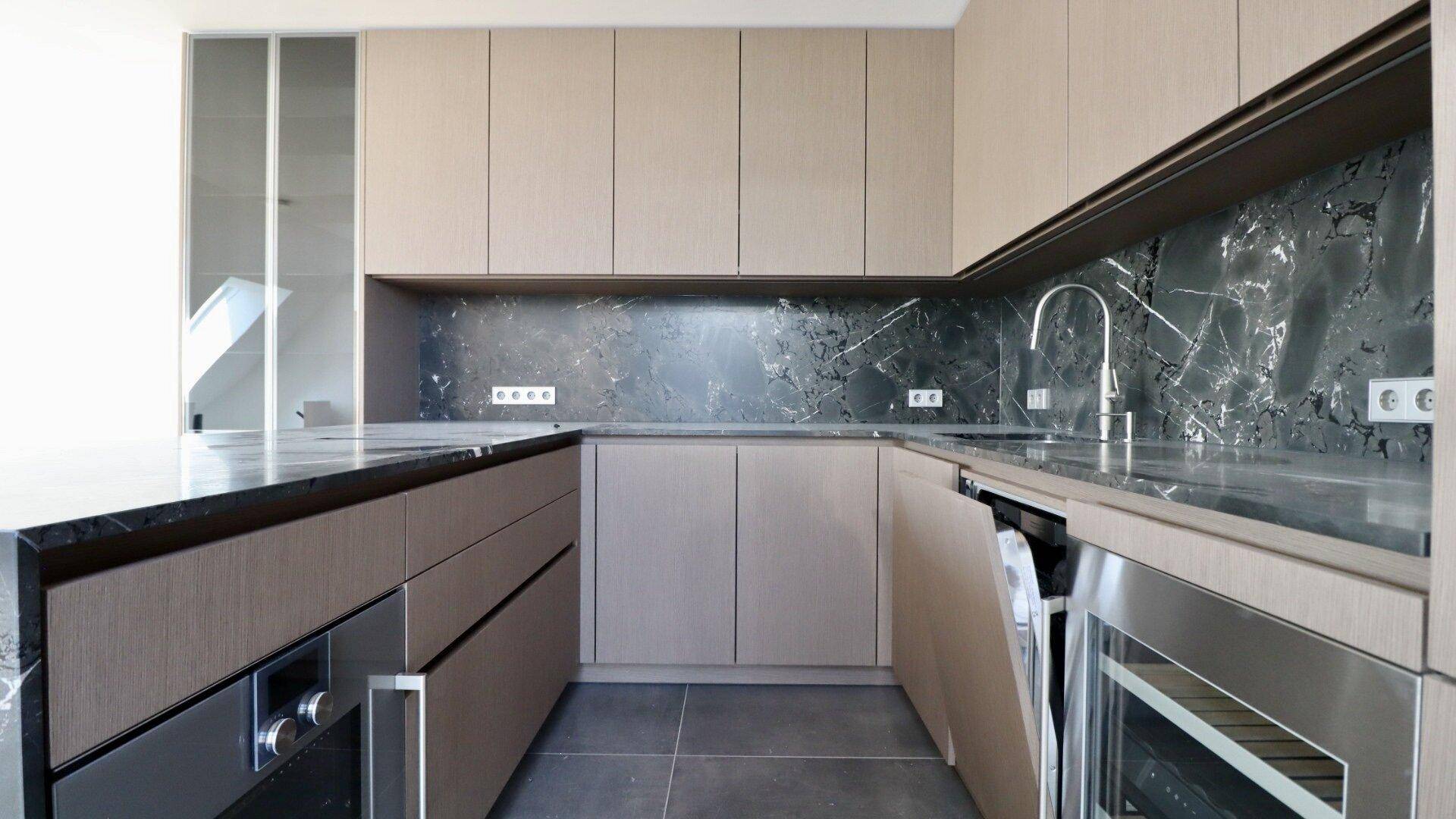 Moderne Einbauküche mit beigen Schränken, dunkler Arbeitsplatte und integrierten Premium-Geräten.