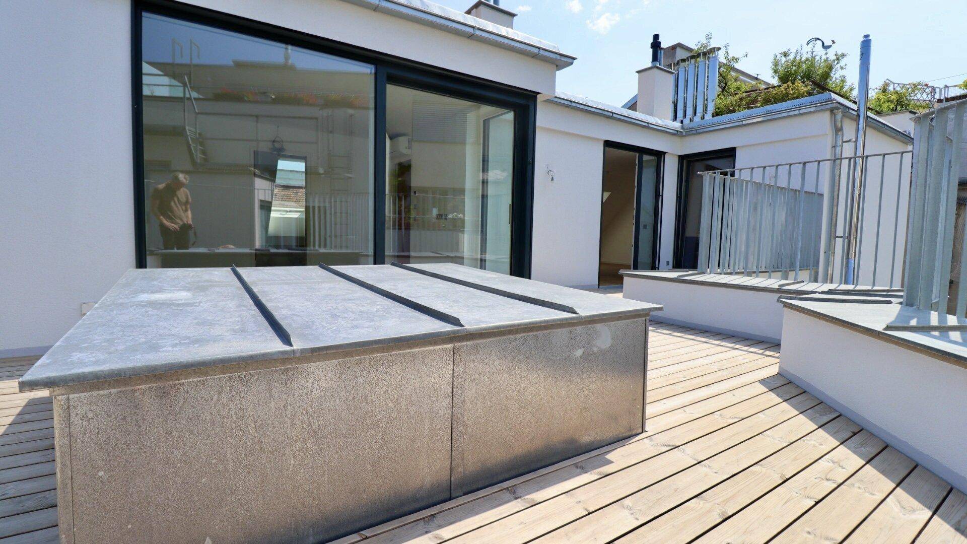 Weitläufige Dachterrasse mit Holzdielen und Blick auf die umliegenden Gebäude unter blauem Himmel.