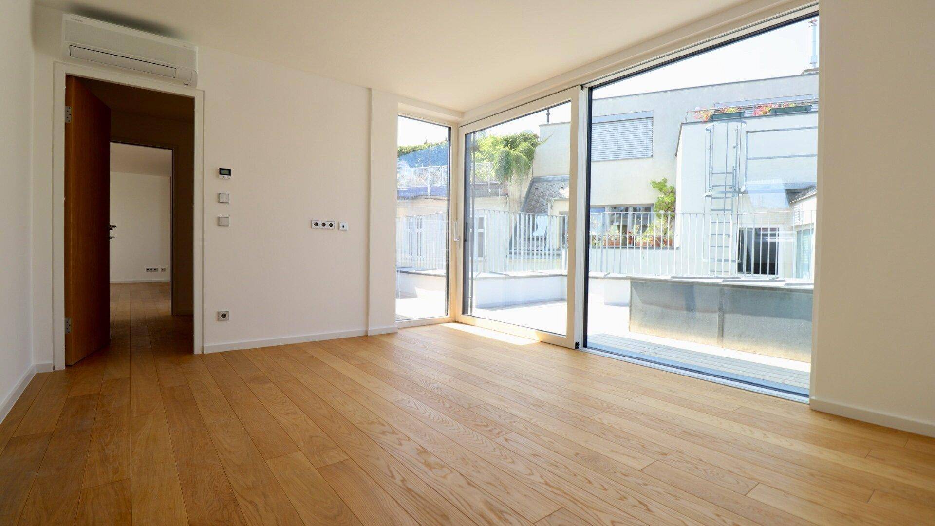 Heller Raum mit Holzboden, großen Schiebetüren zur Terrasse und Klimaanlage für Komfort.