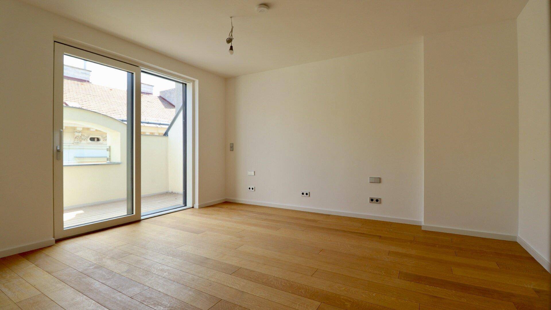 Heller Raum mit Holzboden und großem Schiebetürfenster, das Zugang zu einem Balkon bietet.