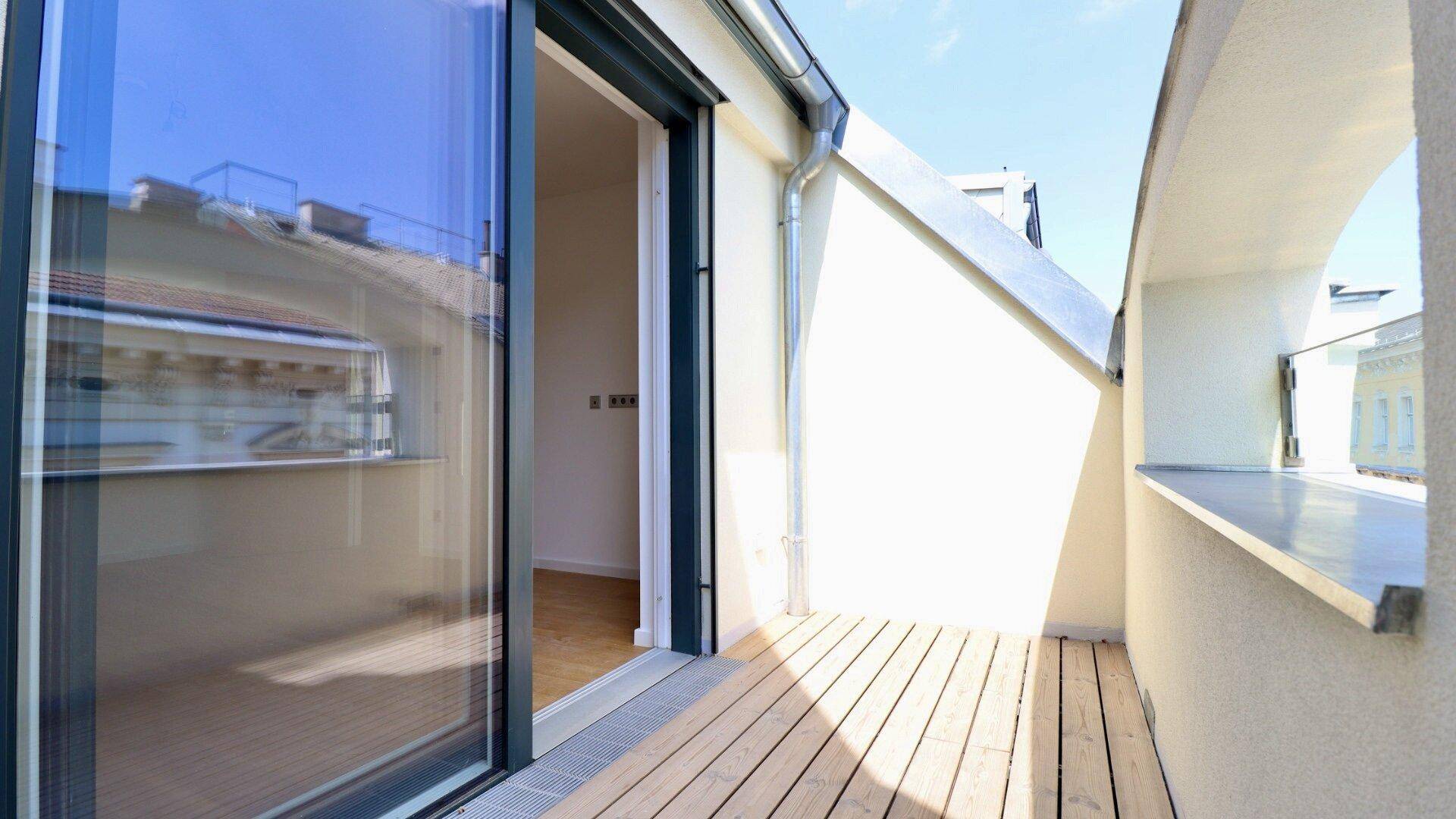 Schmaler Balkon mit Holzdielen und Zugang durch eine Glasschiebetür, bietet einen Blick auf die Umgebung.