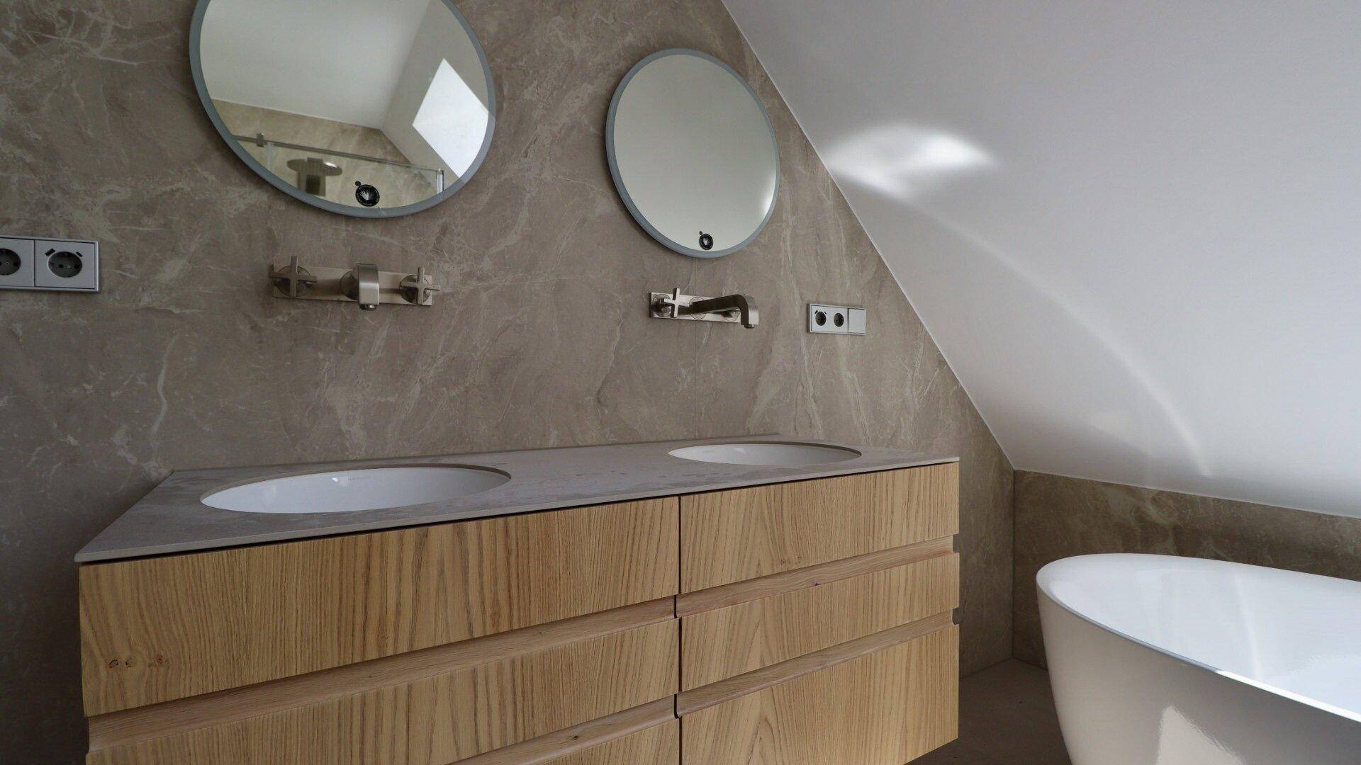 Elegantes Badezimmer mit Doppelwaschbecken, runden Spiegeln und Marmorfliesen unter der Dachschräge.