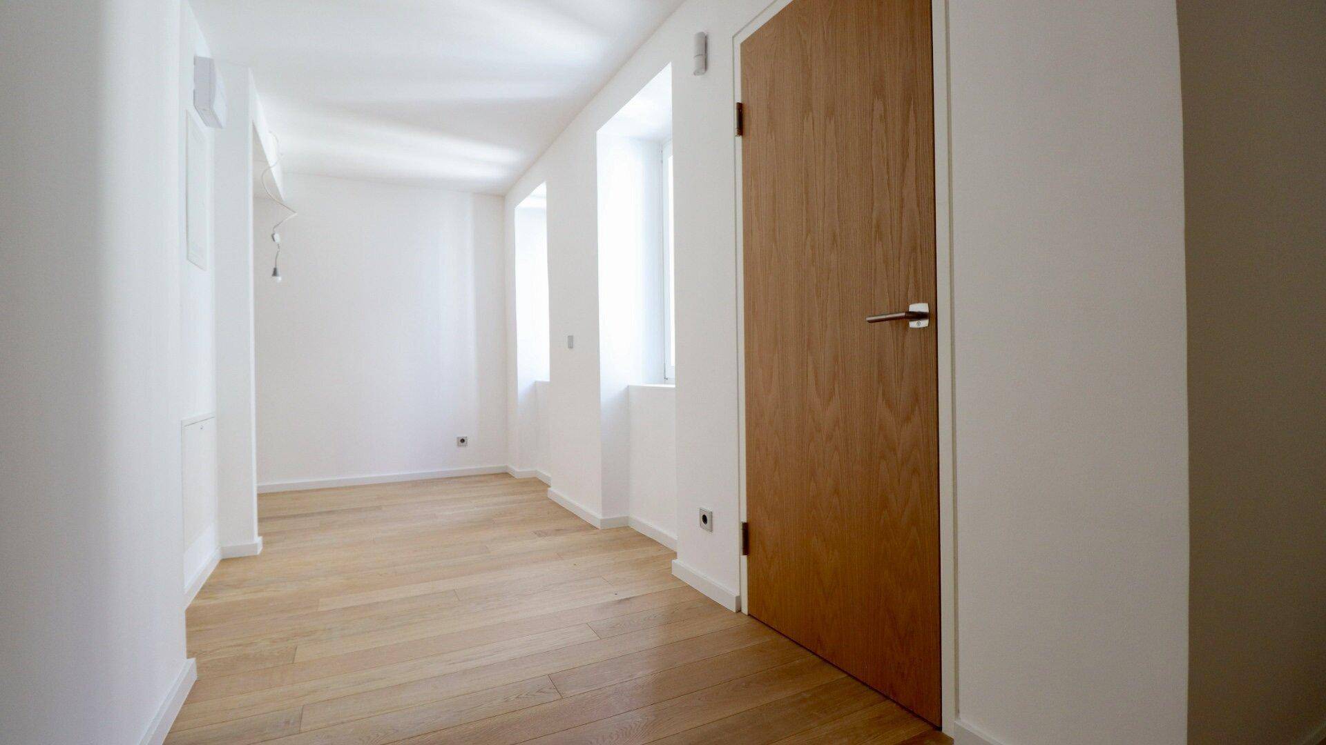 Heller Flur mit Holzboden und hohen Fenstern, der zu weiteren Räumen im Haus führt.